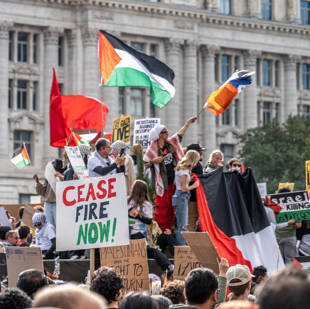Protesters on the street holding Palestine flag and 'cease-fire now' banners